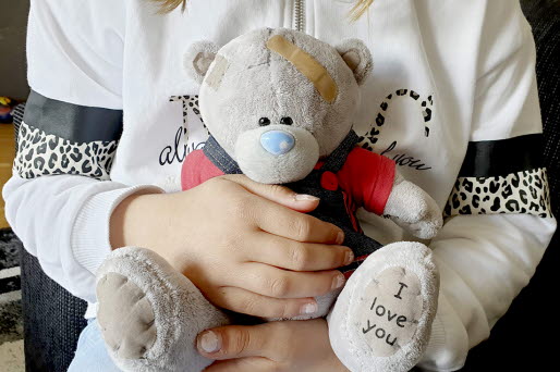 Ett barn håller i sin nallebjörn. Nallebjörnen har ett plåster i pannan.
