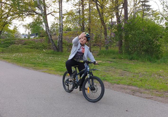 Ett barn på cykel vinkar.