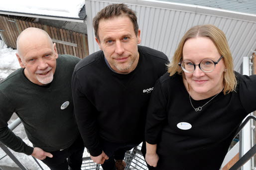 Tre personer står på en spiraltrappa utomhus och tittar uppåt mot kameran.