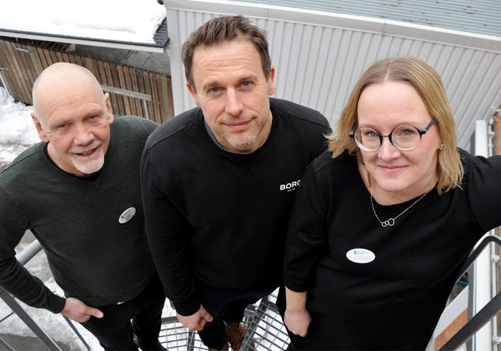 Tre personer står på en spiraltrappa utomhus och tittar uppåt mot kameran.