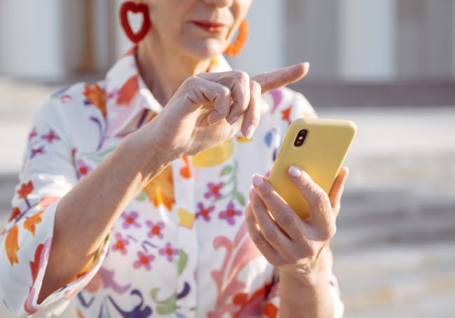 Äldre kvinna scrollar på telefon.