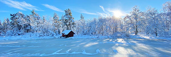 Vy över vinterlandskap med en röd stuga i horisonten.