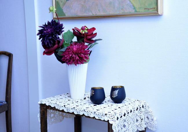 Ett litet bord med en vas med stora blommor i samt två värmeljus.