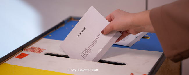 Närbild på när en person stoppar ett valkuvert i valurnan.