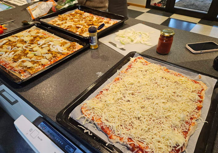 Flera plåtar med pizza, redo att bakas.