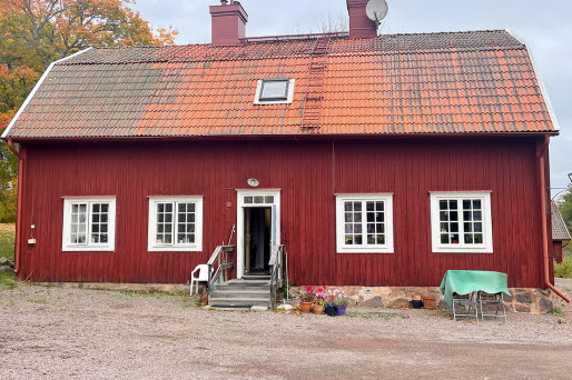 Framsidan av huset. Ett rött trähus med röd tegel.
