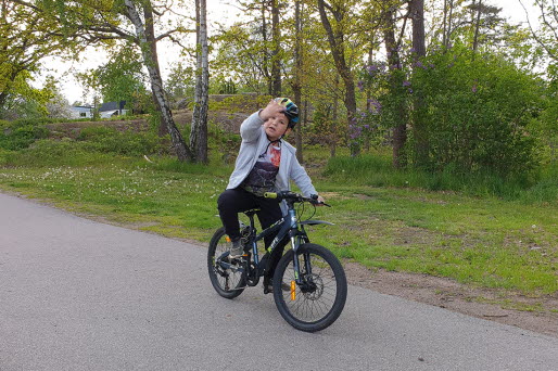Ett barn på cykel vinkar.