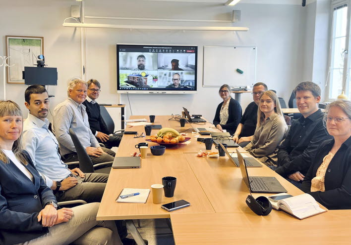 En grupp personer sitter i möte vid ett avlångt bord.