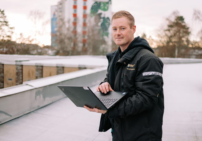 Daniel står utanför en byggnad med sin dator i handen.