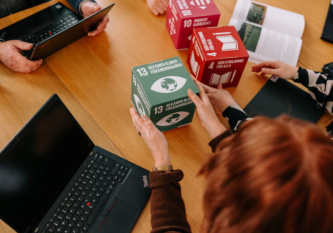 Möte där man ser närbild på deltagare som håller i klossar med budskap från Agenda 2030.
