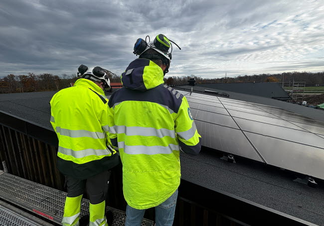 Två personer inspekterar en takkonstruktion och solcellsanläggning.