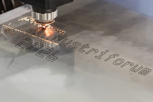 En laser skriver texten Industriforum 2026 på en mettalbit.