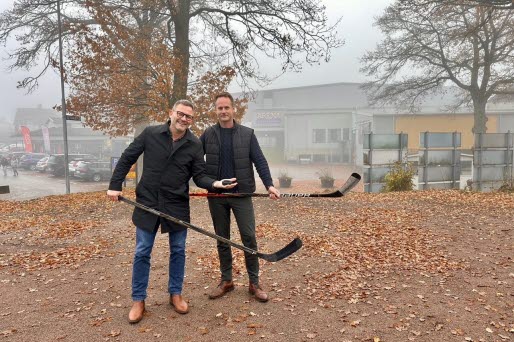 Två personer med hockeyklubbor i händerna på en grusad yta.