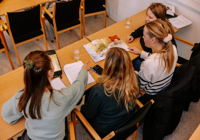 Individer sitter vid ett bord och pekar på en bok